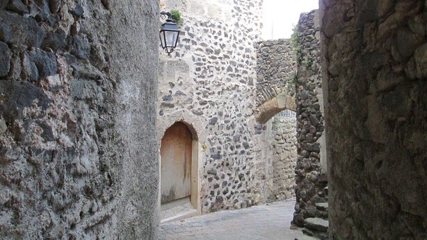 An ancient stone building with a narrow passageway, a lantern, and an arched doorway.