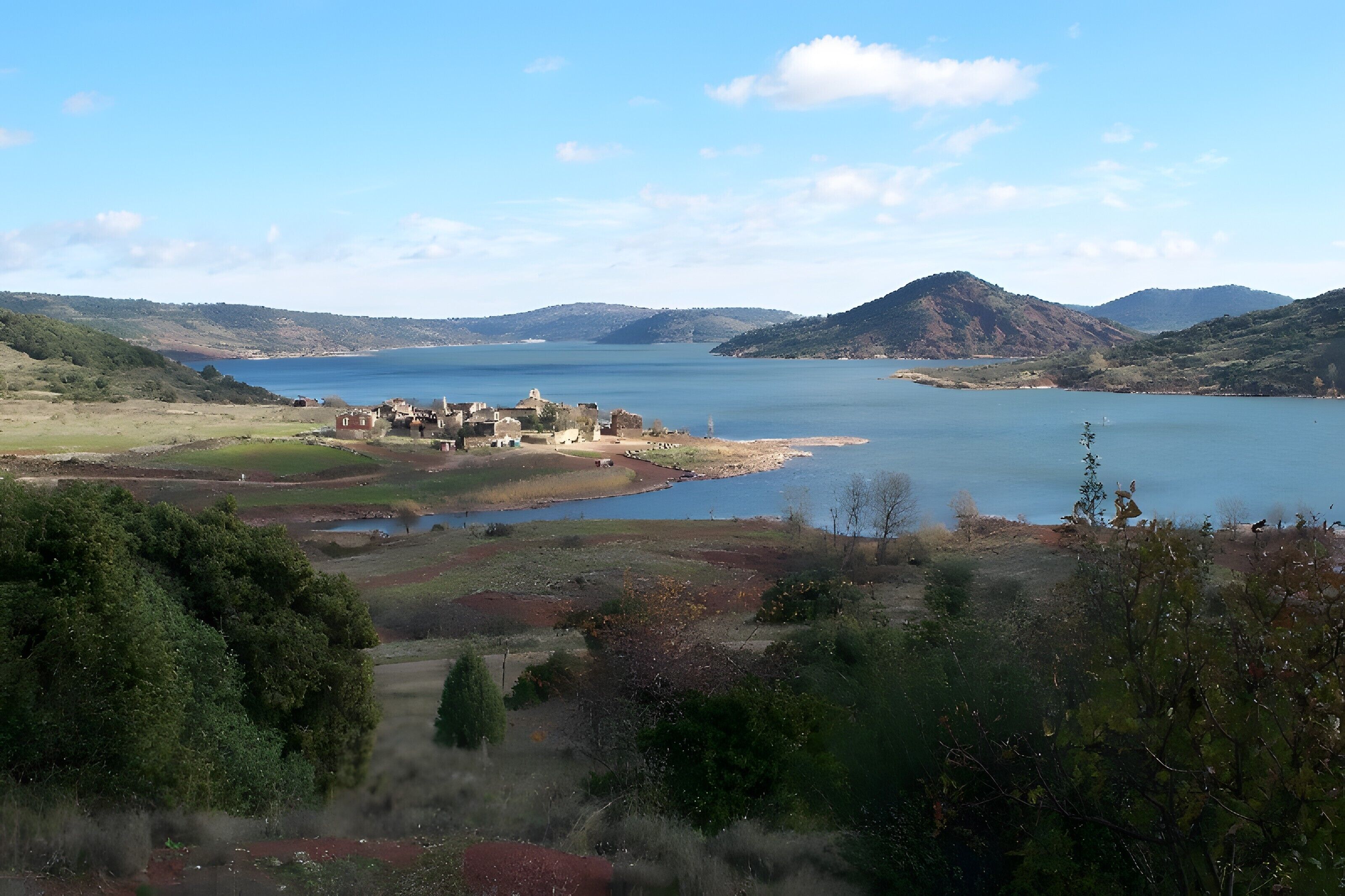 A coastal landscape with a small settlement, hills, and a body of water.