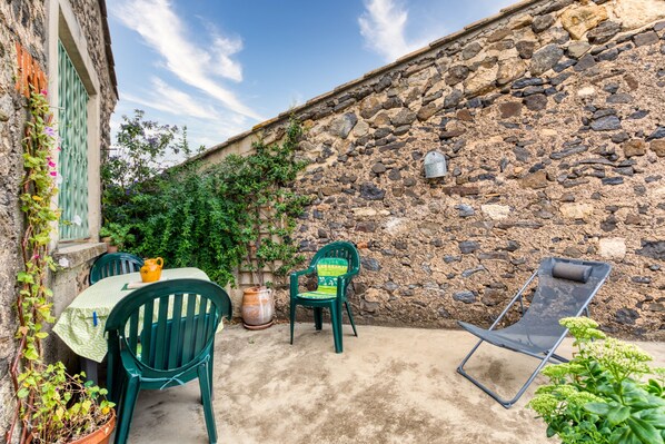 Un muro de piedra, una mesa con sillas y una tumbona en un patio al aire libre.