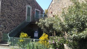 Un edificio de piedra con una escalera de metal, rodeado de follaje y una cerca metálica.