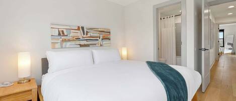 Una habitación de hotel moderna con una cama grande, una mesita de noche con lámpara, un ventilador de techo y un cuadro en la pared.