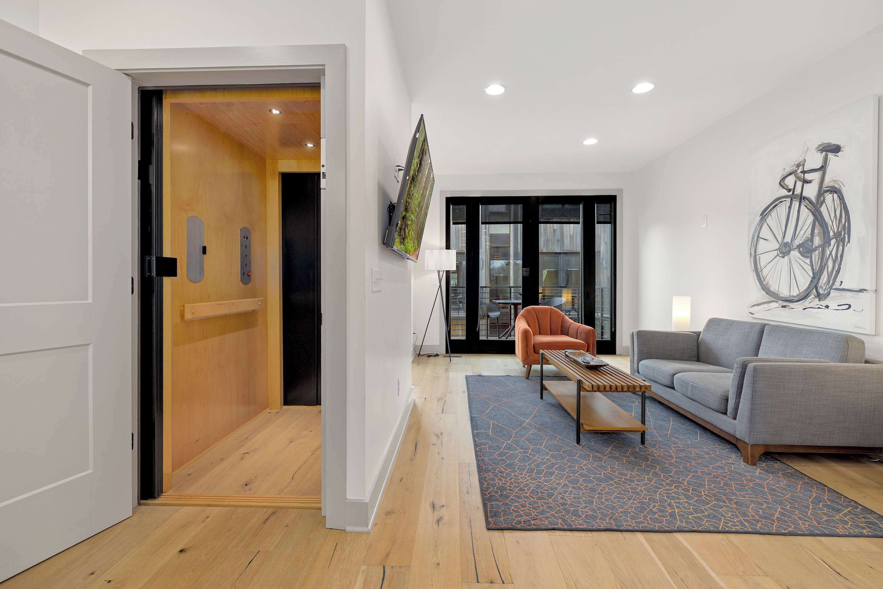 Una sala de estar moderna con puerta de madera, un sofá gris, una mesa de centro de madera y un tapete azul.
