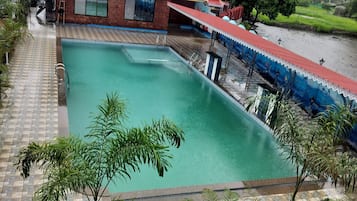A swimming pool with a tiled deck, surrounded by palm trees and a building with a red roof.