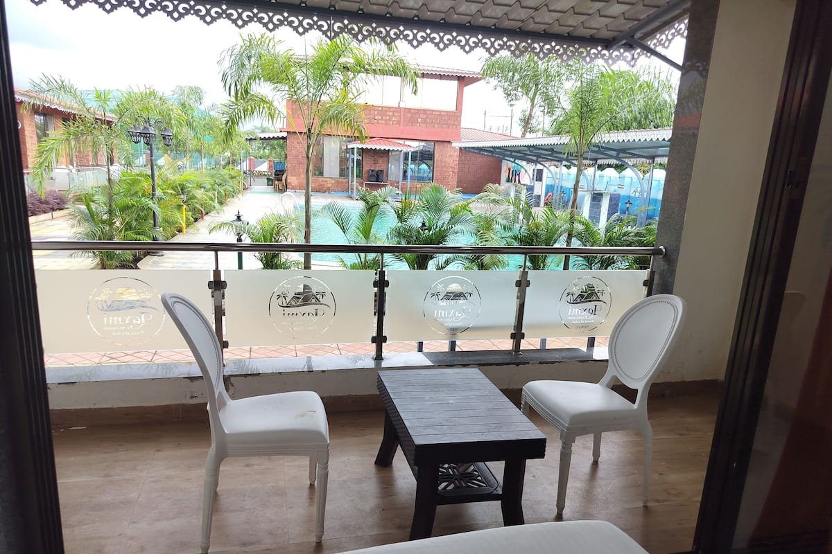 Un balcon avec deux chaises blanches et une petite table, donnant sur une piscine et une végétation luxuriante.