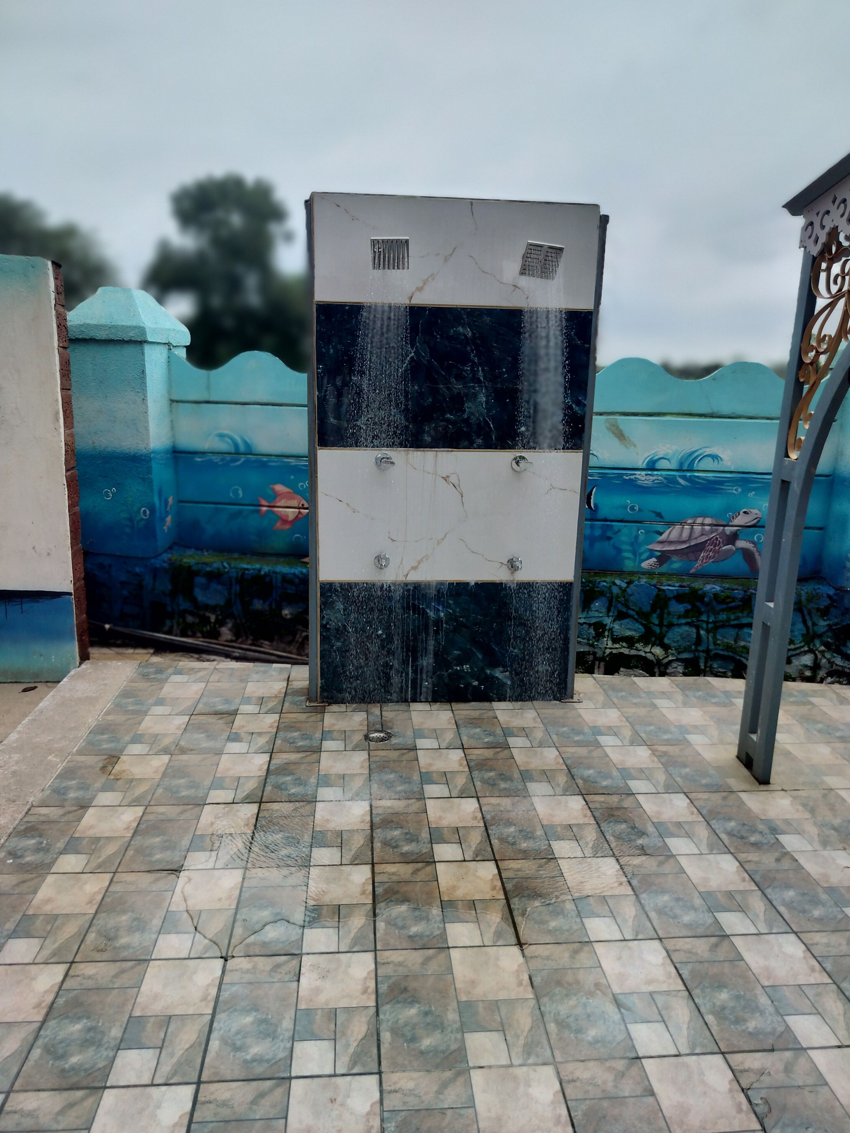 Des toilettes publiques avec un sol carrelé en bleu et blanc, une fresque représentant une tortue sur le mur et une main courante en métal sur le côté droit.