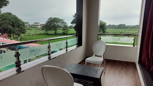 A balcony with a view of a green landscape, a railing, and two white chairs and a table. - Sandalwoods Resorts (Karjat)