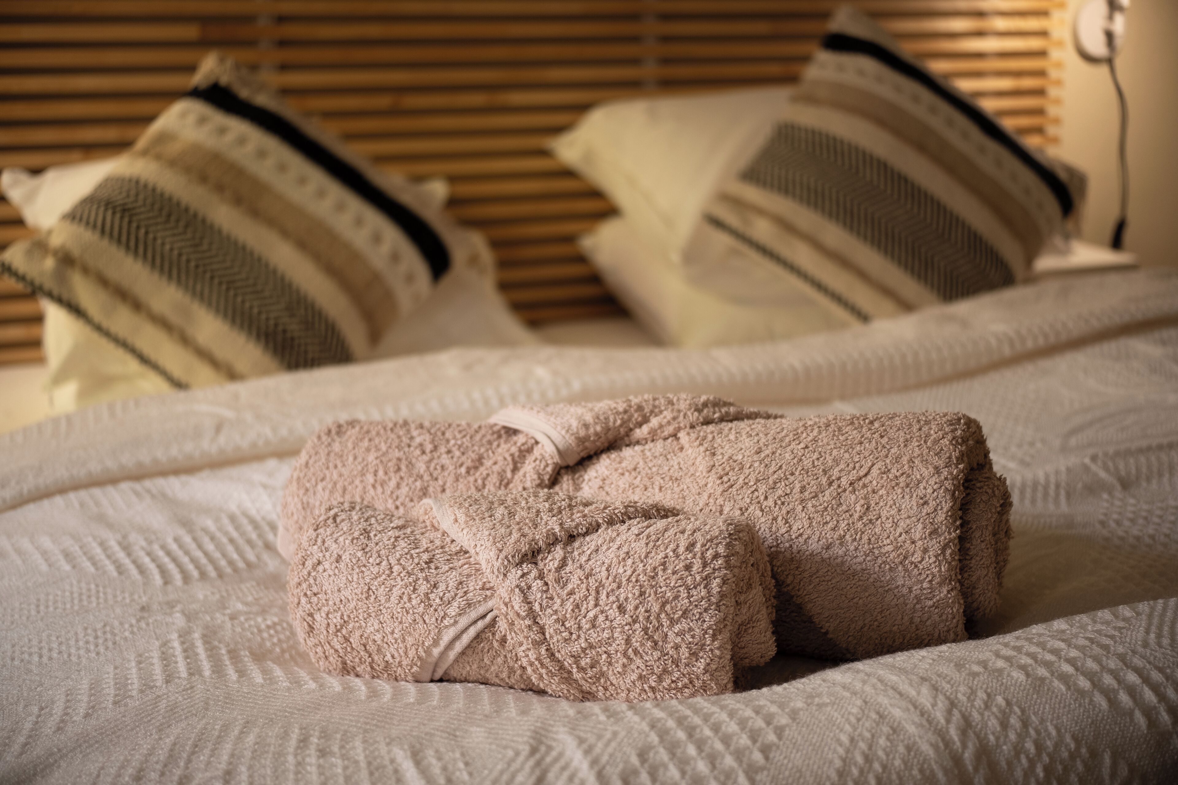 A neatly made bed with a folded towel, a pillow with a striped pattern, and a pillow with a chevron pattern.