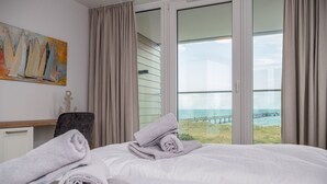 Een hotelkamer met een bed, een schilderij aan de muur en uitzicht op de zee door het raam.