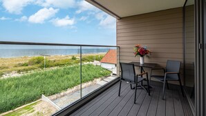 Een balkon met uitzicht op zee, een tafel met stoelen en een vaas met bloemen.