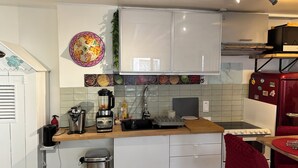 Eine kleine Küche mit weißen Schränken, einer Holz Arbeitsplatte, einem Mixer, einem Wasserkocher und einem roten Kühlschrank.
