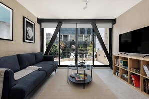 A modern living room with a dark sofa, a glass coffee table with books, a TV on a wooden shelf, and a balcony with outdoor furniture. - w* |Fabulous Loft near Angel De Independencia (Ciudad de México)
