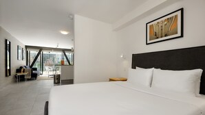 Une chambre d’hôtel moderne dotée d’un grand lit, offrant une vue sur l’extérieur et comprenant un coin repas visible à travers une paroi en verre.