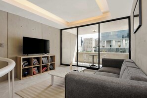 A modern living room with a flat-screen TV, a bookshelf, a sofa, and a balcony with a view of buildings.