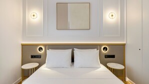 A hotel room with a large bed, two bedside tables, a wall-mounted light fixture, and a small round table. - Michalakopoulou Cover & Bright Apartment (Athens)