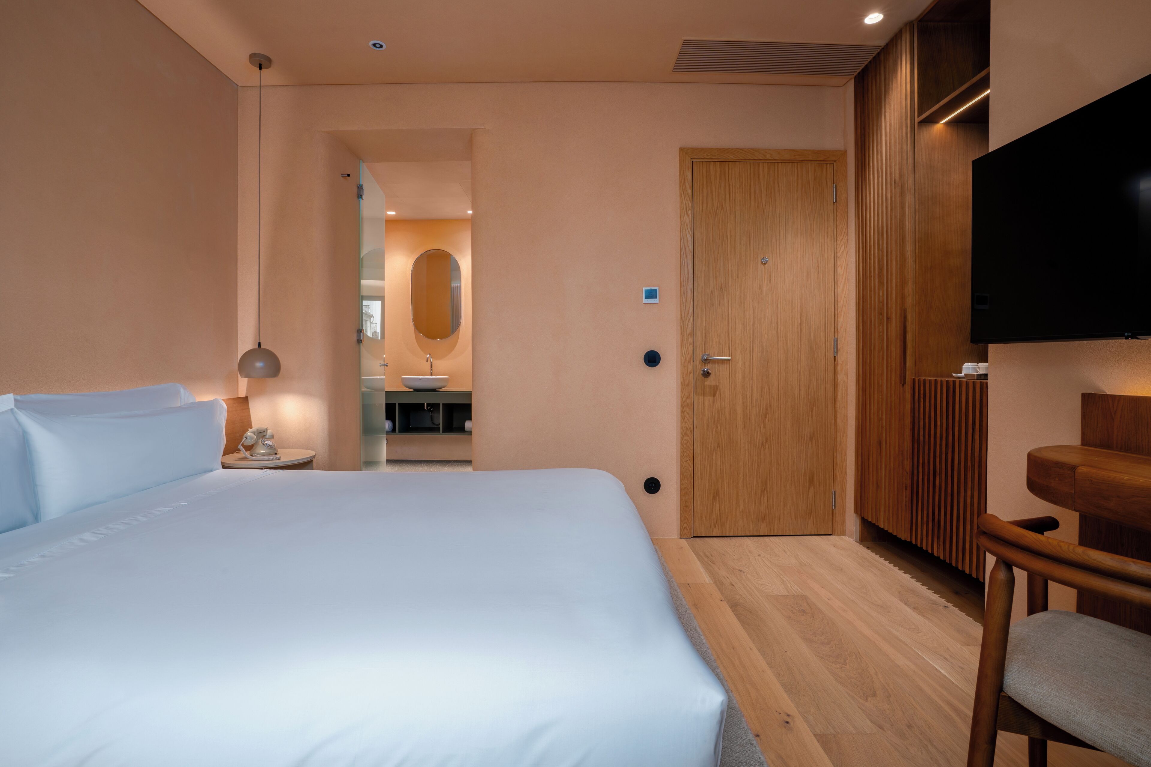 Una camera d'albergo con un letto grande, un armadio in legno, una televisione e un tavolino con una lampada.