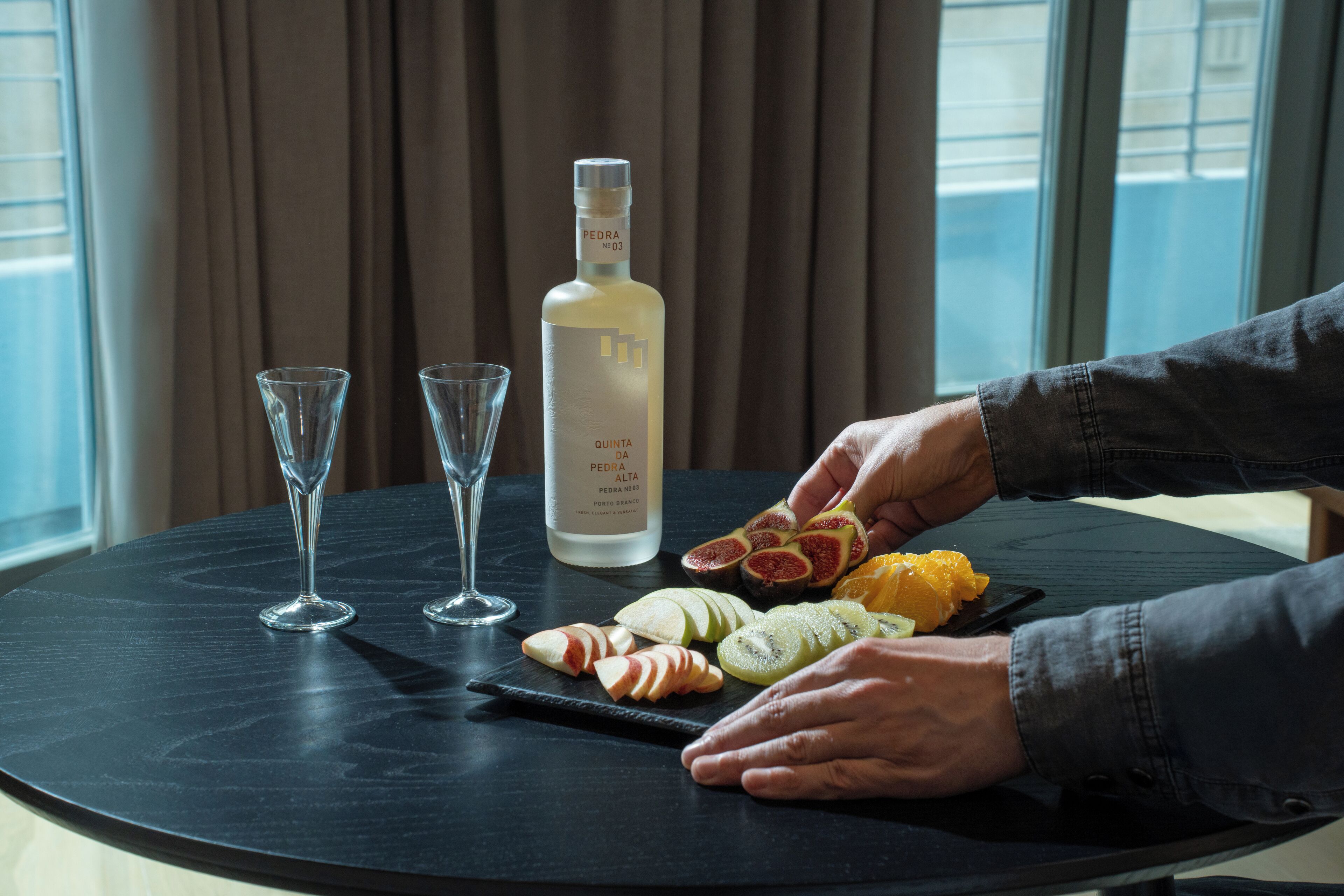 Een tafel met een fles drank, twee glaasjes en gesneden fruit.