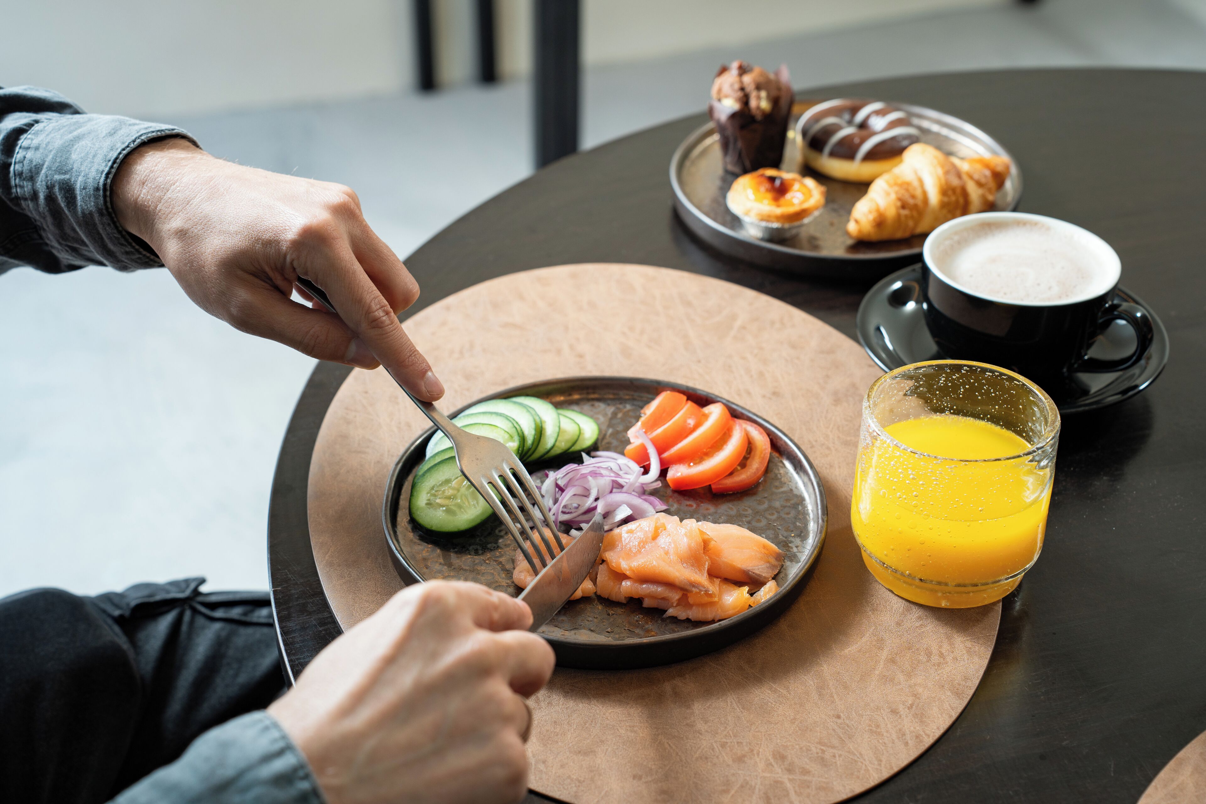 A breakfast setting with a plate of salmon, vegetables, and a glass of orange juice on a round table.