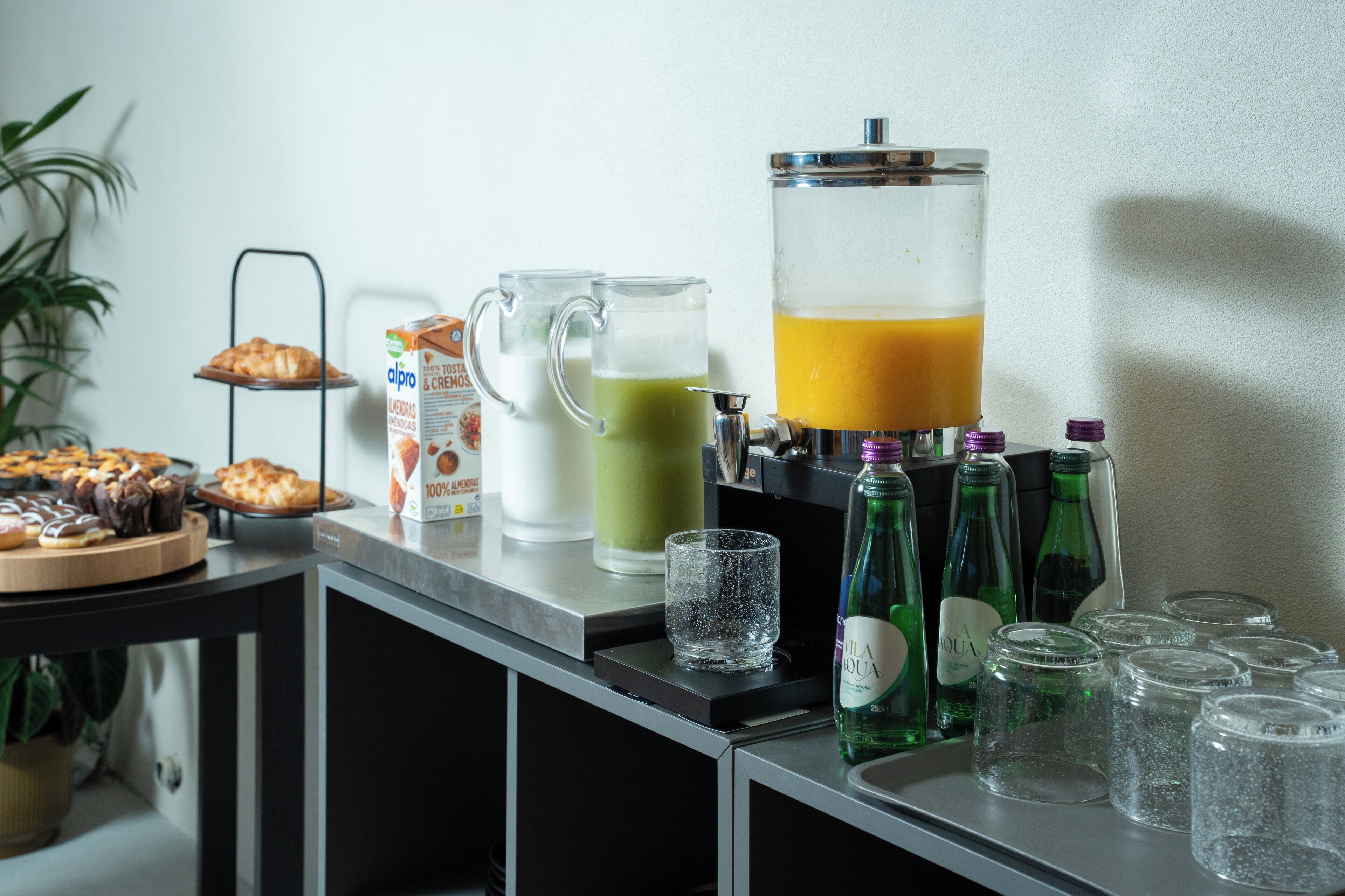 A breakfast bar with a variety of food items, a juice dispenser, and several empty glasses.