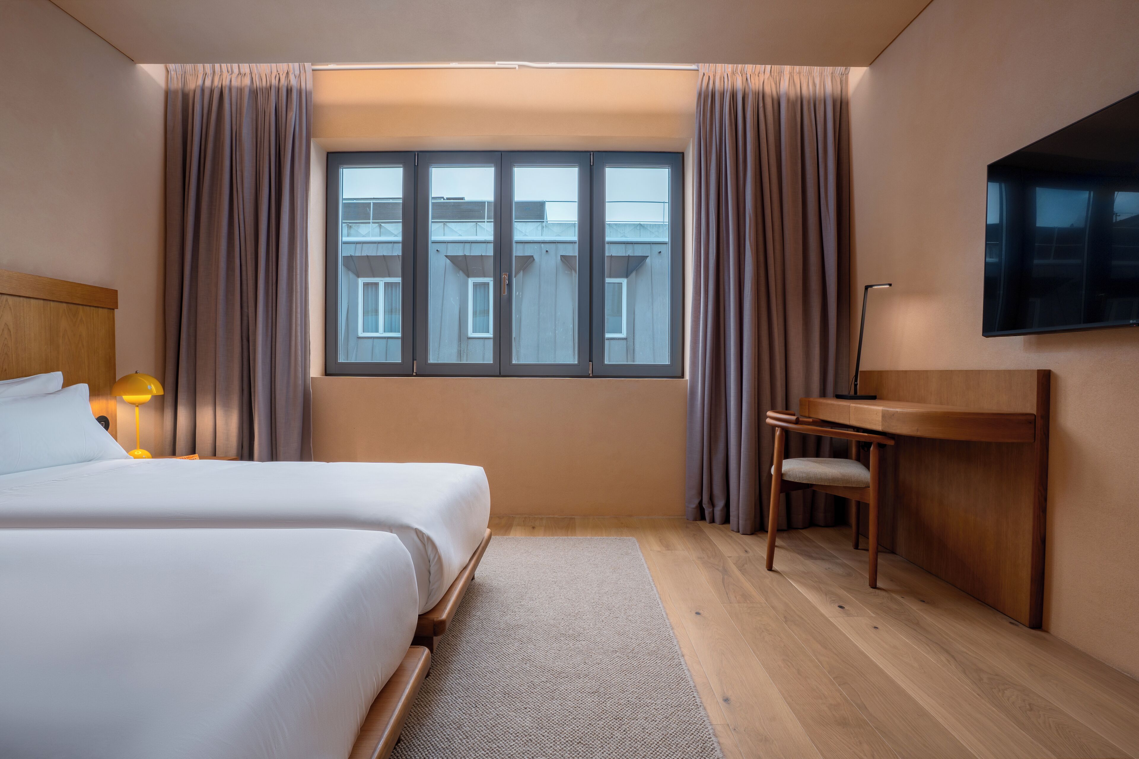 Habitación de hotel con dos camas, un escritorio, una silla, un televisor y una ventana con cortinas.