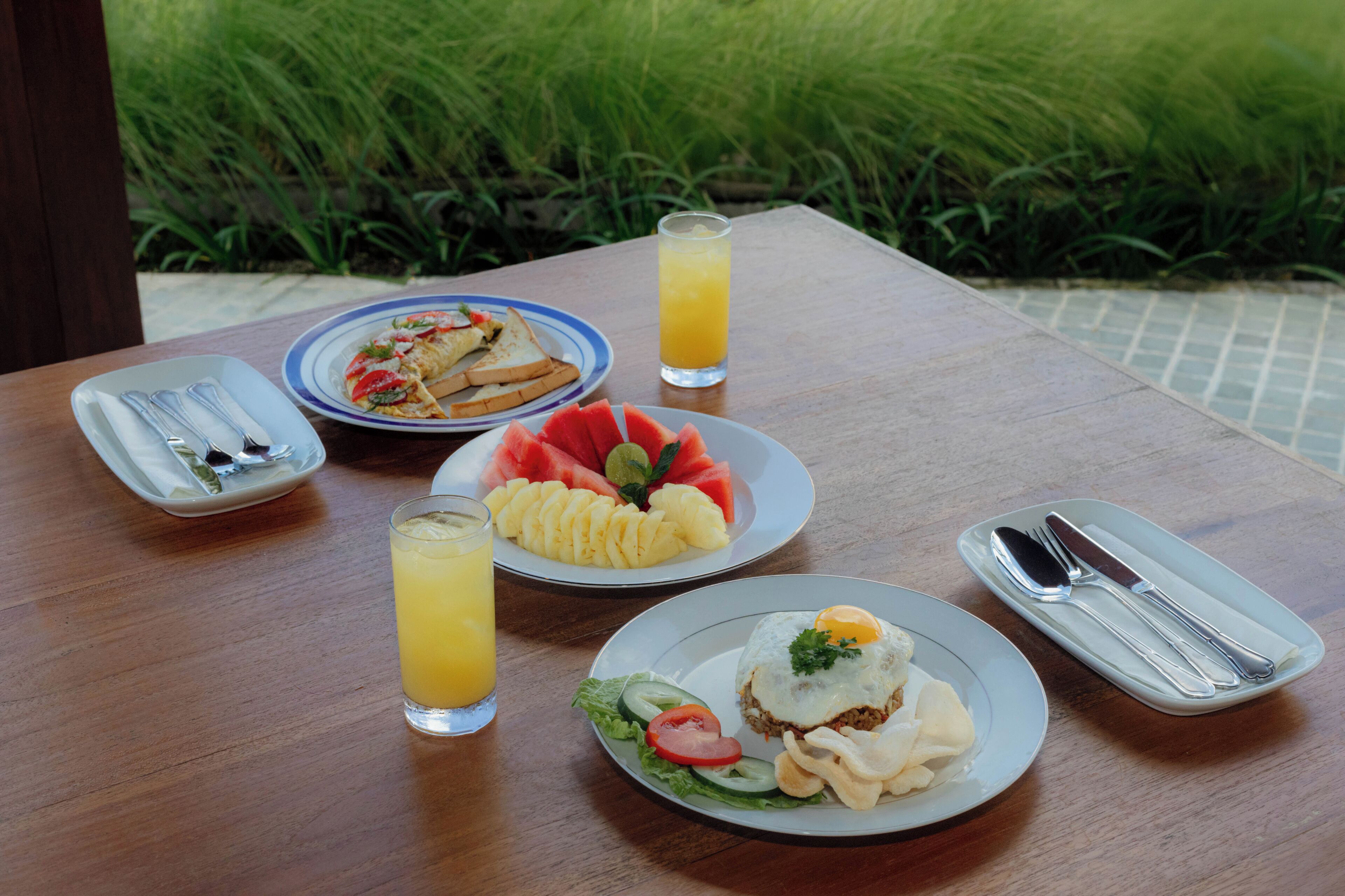 A wooden table with plates of food, a glass of orange juice, and cutlery.