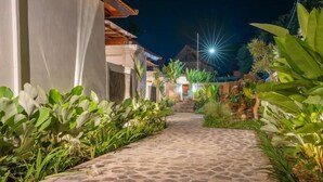 A pathway leading to a building with a stone floor and lush greenery on both sides. - Tumbu Retreat (Karangasem)