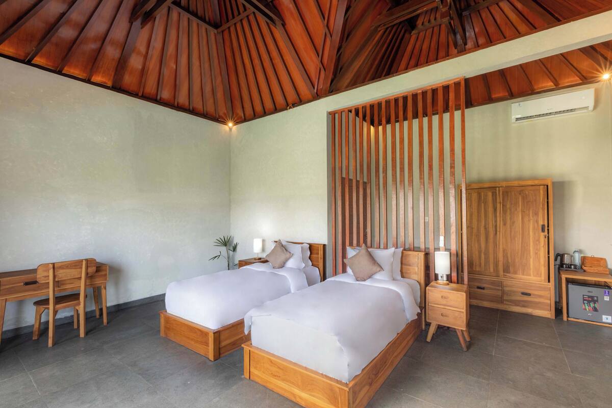 A hotel room with two wooden beds, a desk, a wardrobe, and a small kitchenette.