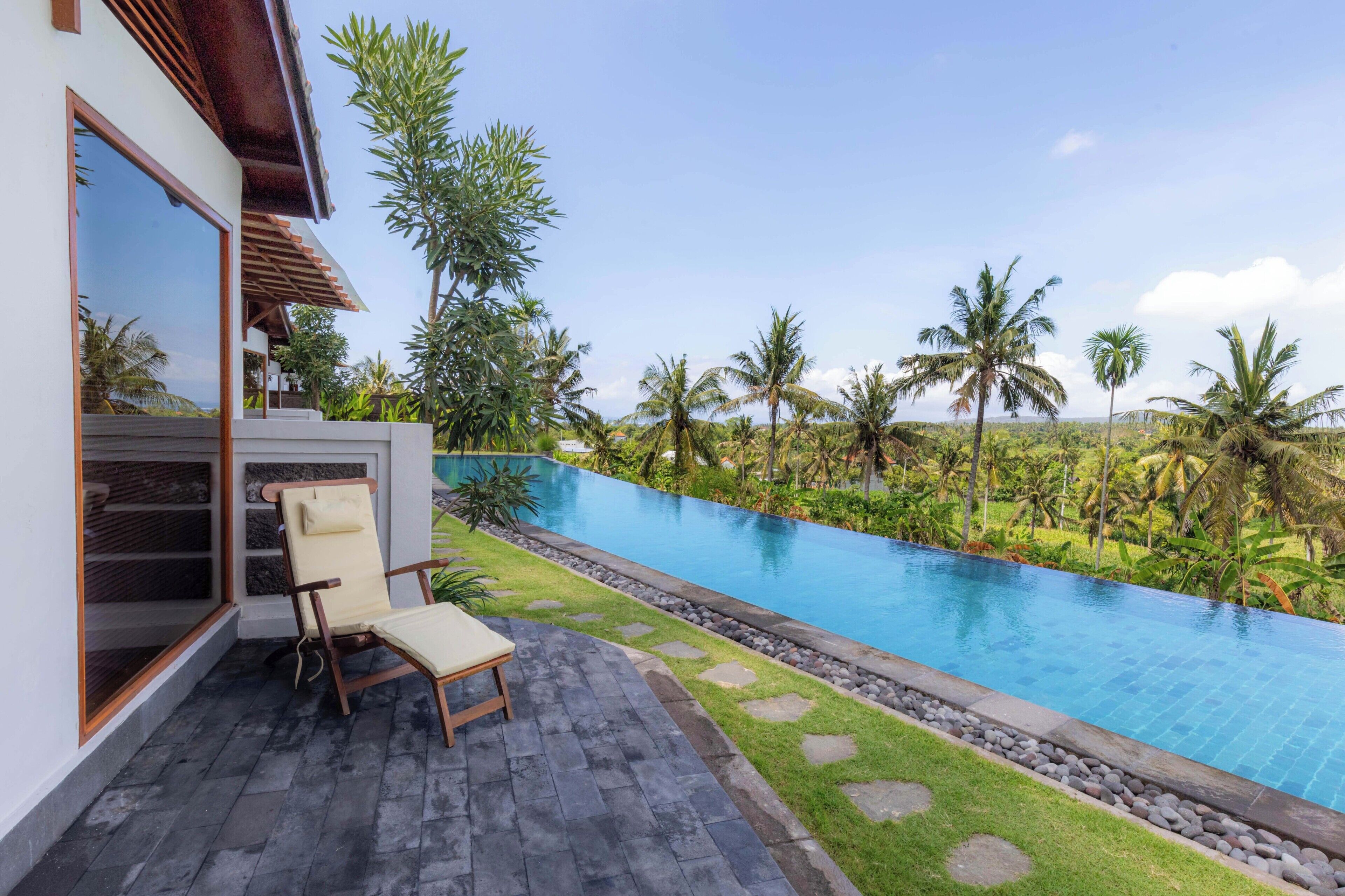 Un área de piscina moderna con una silla de descanso y vistas a un paisaje tropical.