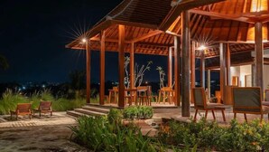 A wooden pavilion with a covered seating area, surrounded by greenery and a view of the night sky. - Tumbu Retreat (Karangasem)