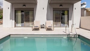 A modern building with a pool, two lounge chairs, and a small table with a cup. - Neaira Apartments (Platanias)