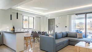 A modern living space with a kitchen island, seating area, and large windows. - Neaira Apartments (Platanias)
