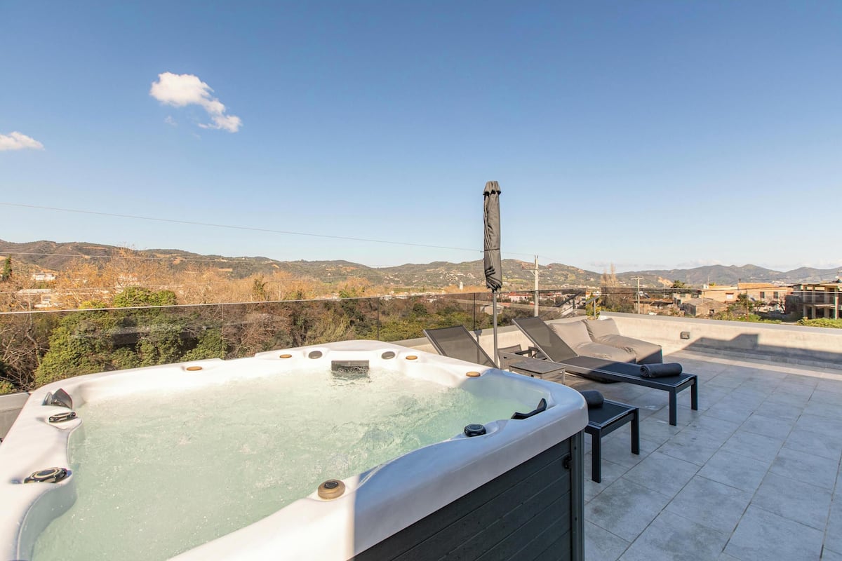 Una terraza en la azotea con un jacuzzi, sillones de descanso y una vista panorámica de las colinas.