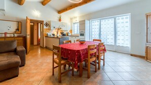 Un vaste espace de vie doté d’un plafond en bois, d’une table à manger avec des chaises, d’un canapé et d’une cuisine à l’arrière-plan.