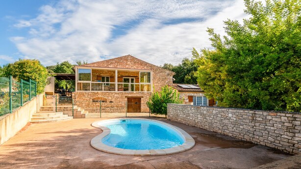 Une maison en pierre avec une piscine, un patio couvert et un mur en pierre.
