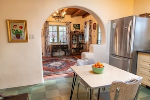 A kitchen with a stainless steel refrigerator, a dining table with a bowl of fruit, and a patterned rug.