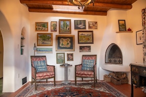 A cozy room with two ornate chairs, a patterned rug, and a collection of framed artworks on the wall.
