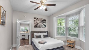 A bedroom with a bed, a ceiling fan, a window with blinds, and a small wooden table. - Masters Classic AUGUSTA (Augusta)