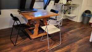 A dining area with a wooden table, two chairs, a laptop, and a small kitchen area with a sink and shelves. - Half-timbered maisonette in Nürtingen (Nürtingen)
