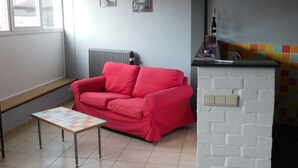 Una sala de estar con un sofá rojo, una mesita, un radiador y un colorido rebozado de azulejos.