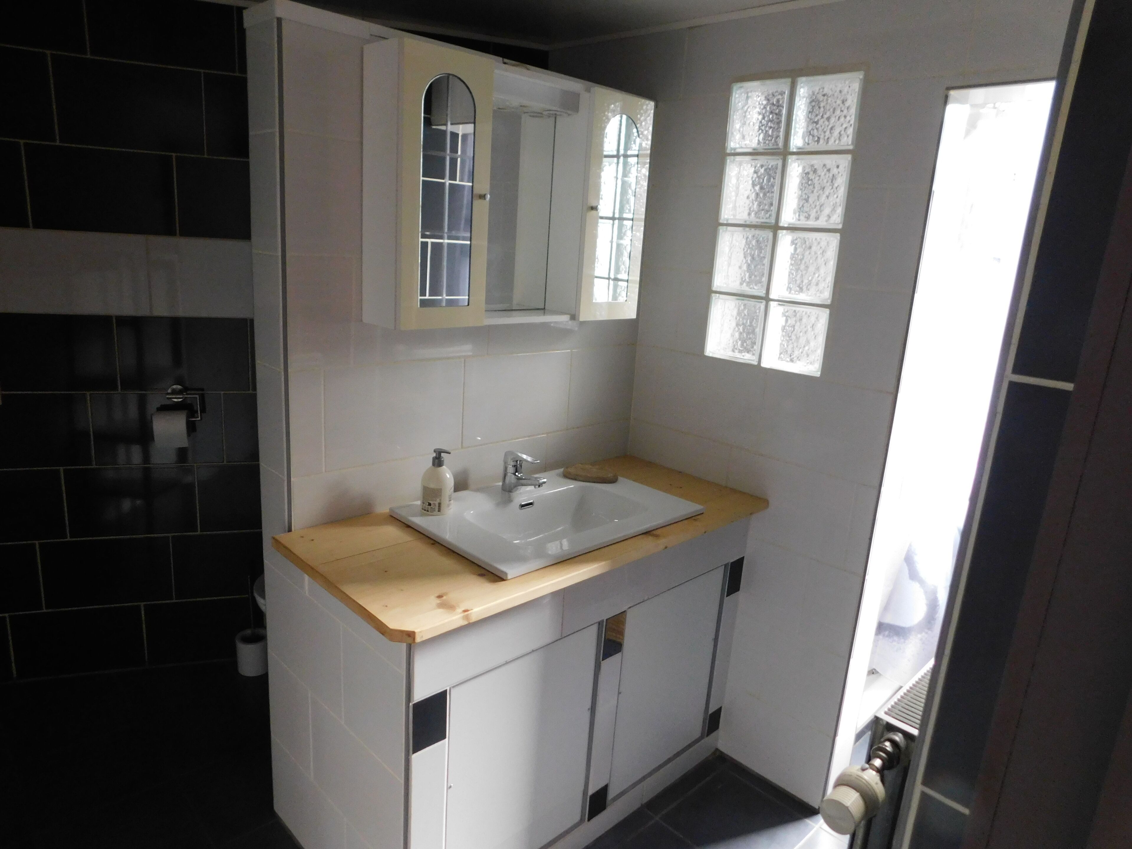 Ein modernes Badezimmer mit einem weißen Waschbecken, einem Spiegel darüber und einem Fenster mit satinierten Glasfeldern.