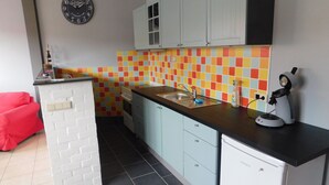 Una cocina compacta con un vibrante salpicadero de azulejos, un reloj en la pared y una silla roja.