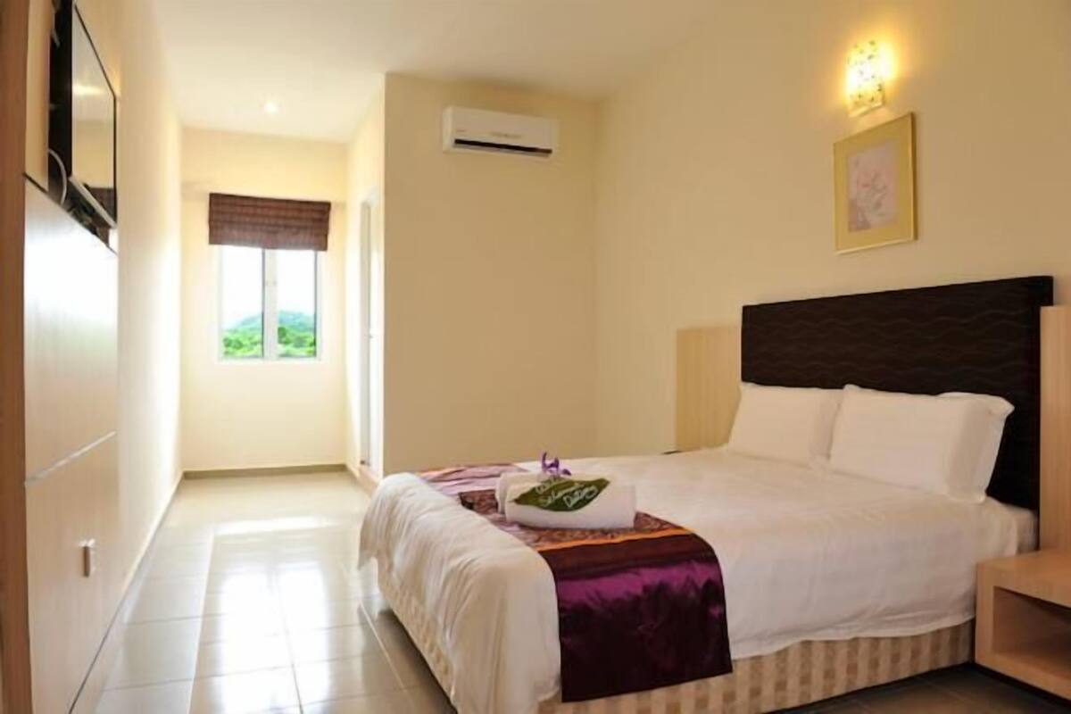 Une chambre d’hôtel comprenant un lit, une table de chevet, une fenêtre avec des rideaux, un appareil de climatisation et un luminaire fixé au mur.