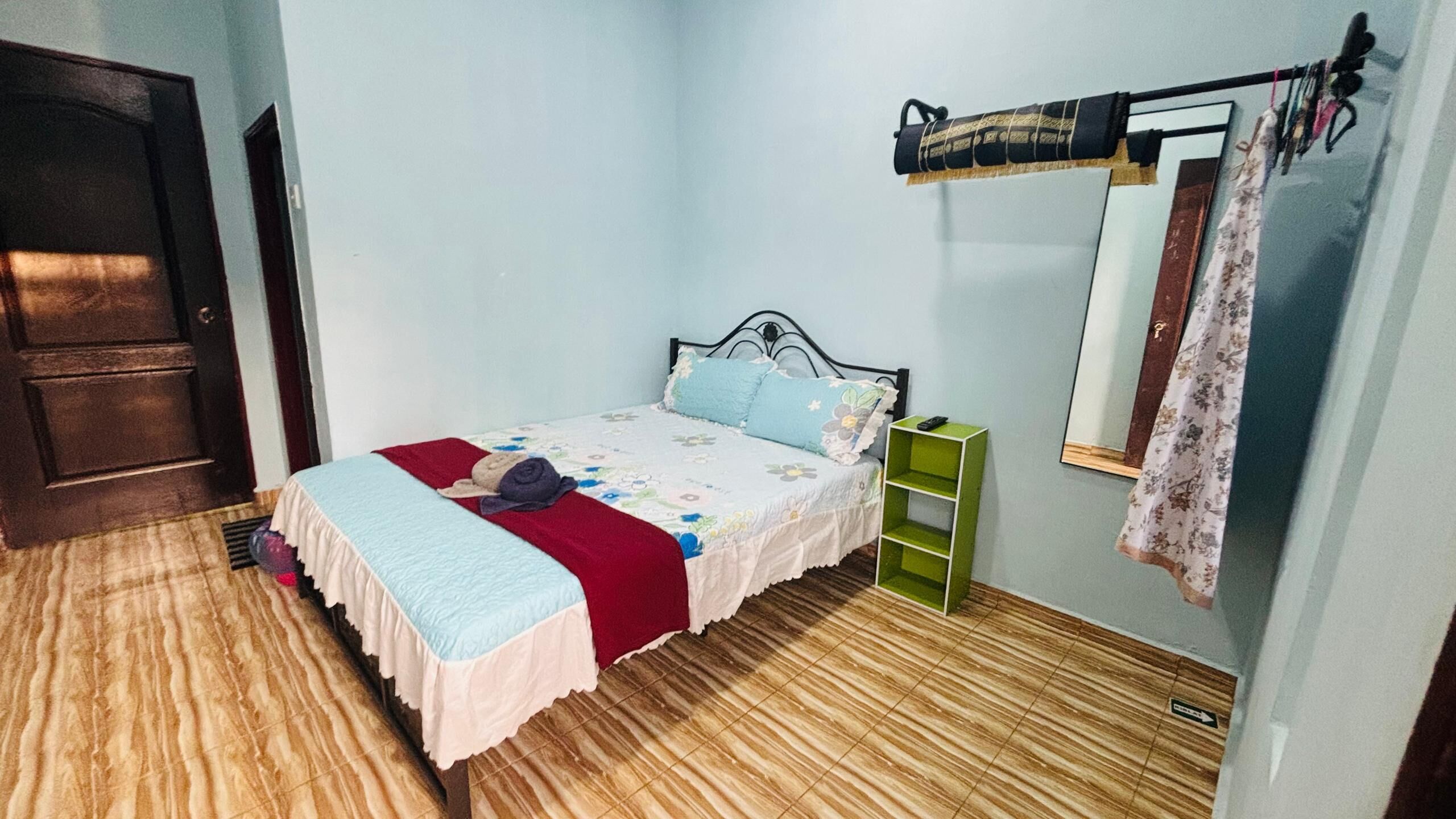 A bedroom with a bed, a green nightstand, a hanging clothes rack, and a door.