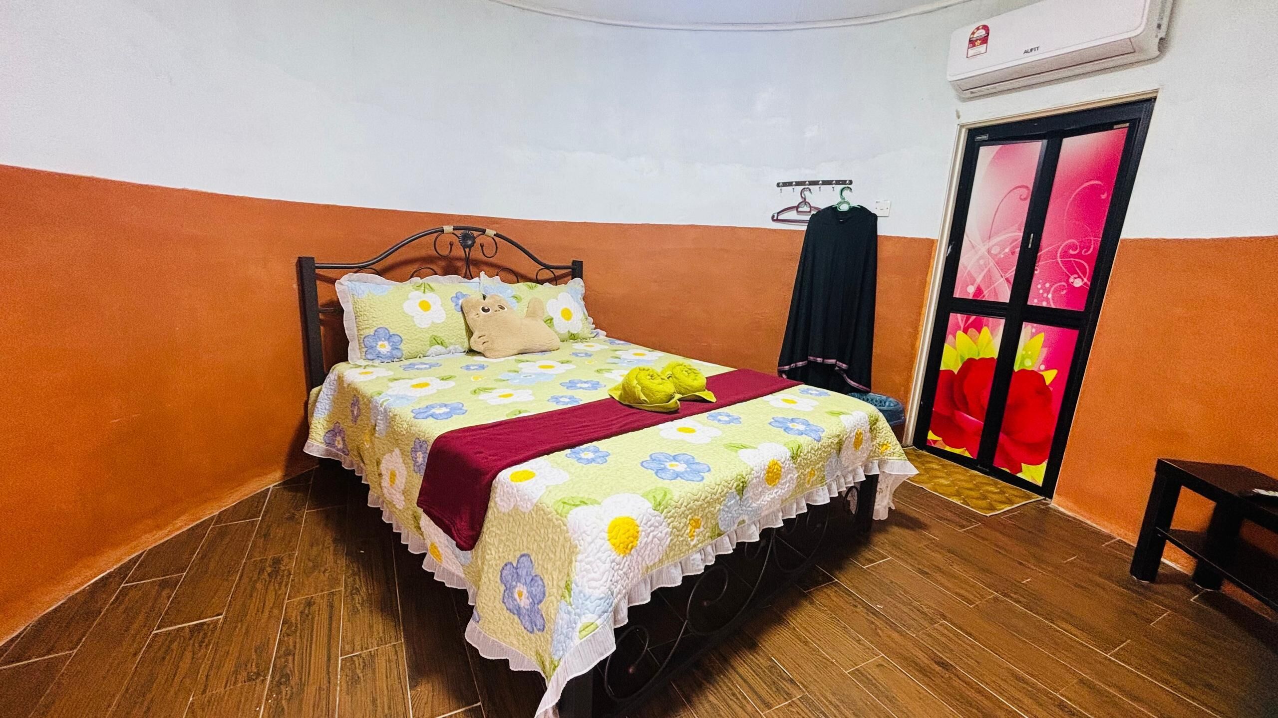 A single bed with a floral bedspread, a red throw blanket, and two green frog-shaped pillows.