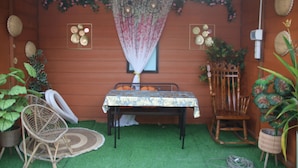 A room with a green artificial turf floor, a table with a patterned tablecloth, wicker chairs, and a rocking chair. - Capital O 91187 D'dusun Raudhah Chalet (Baling)