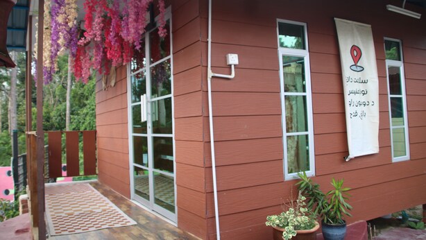 A wooden building with a balcony, potted plants, and a banner with text. - Capital O 91187 D'dusun Raudhah Chalet (Baling)