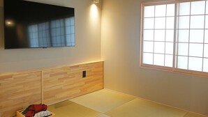 A room with tatami flooring, a mounted TV, a sliding door with a grid pattern, and a wooden panel wall. - Kyomachiya SEN Gojo-Ikkanmachi ANNEX (Kyoto)
