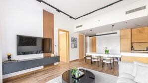 A modern living room with a flat-screen TV, a round coffee table, and a dining area with a white table and chairs. - JVC Gem 2BR w maidsroom - Oakley Square (Dubai)