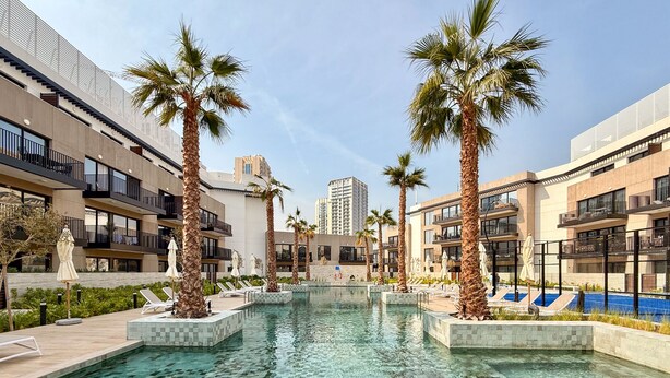 A modern hotel with a central swimming pool surrounded by palm trees and lounge chairs. - JVC Gem 2BR w maidsroom - Oakley Square (Dubai)