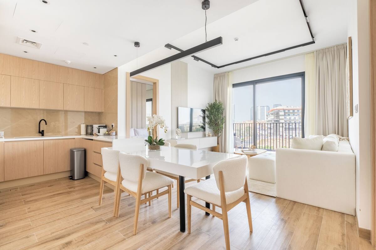 Un espace de vie moderne comprenant un coin repas, une cuisine et une grande fenêtre offrant une vue sur la ville.