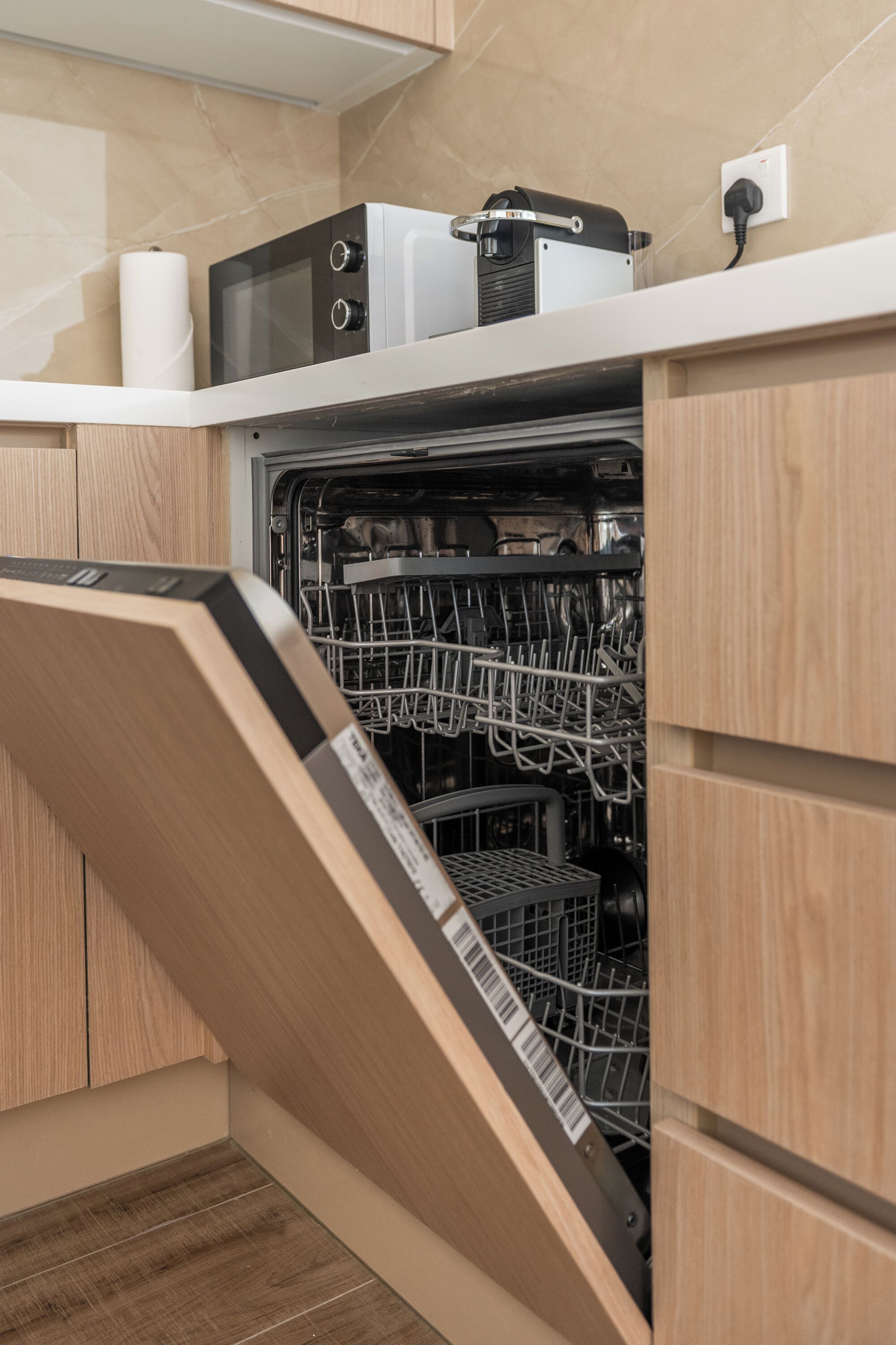 A modern kitchen with a dishwasher, a microwave, and a kettle on the countertop.